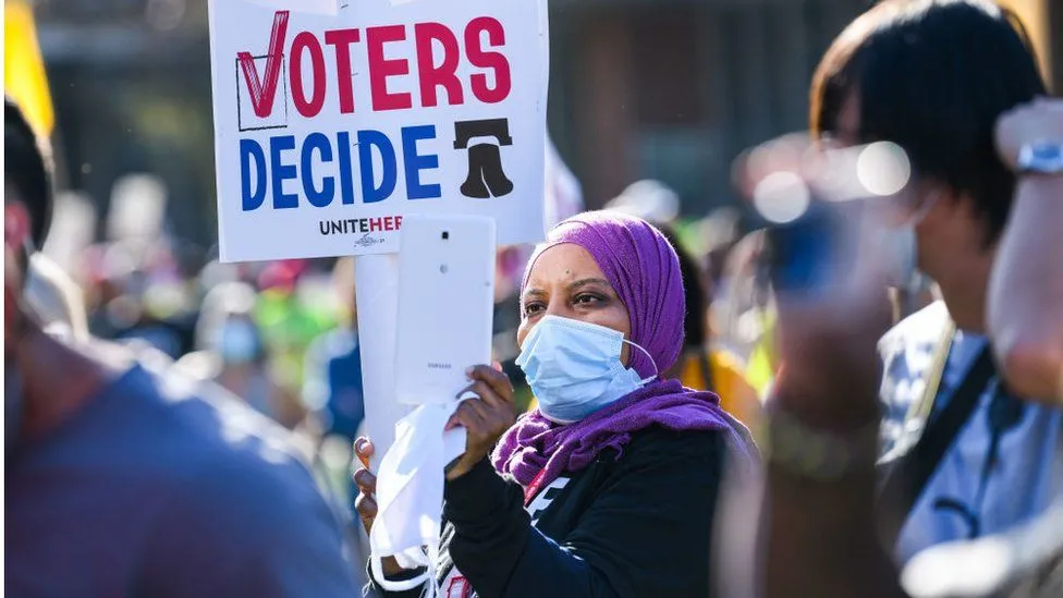 Woman in hijab holding a sign which states Voters Decide